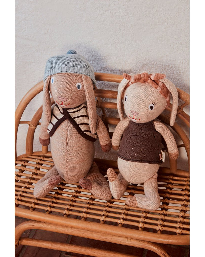 Gebreide knuffel Jolien Rabbit in beige met jurk en hoofdband op rieten stoel