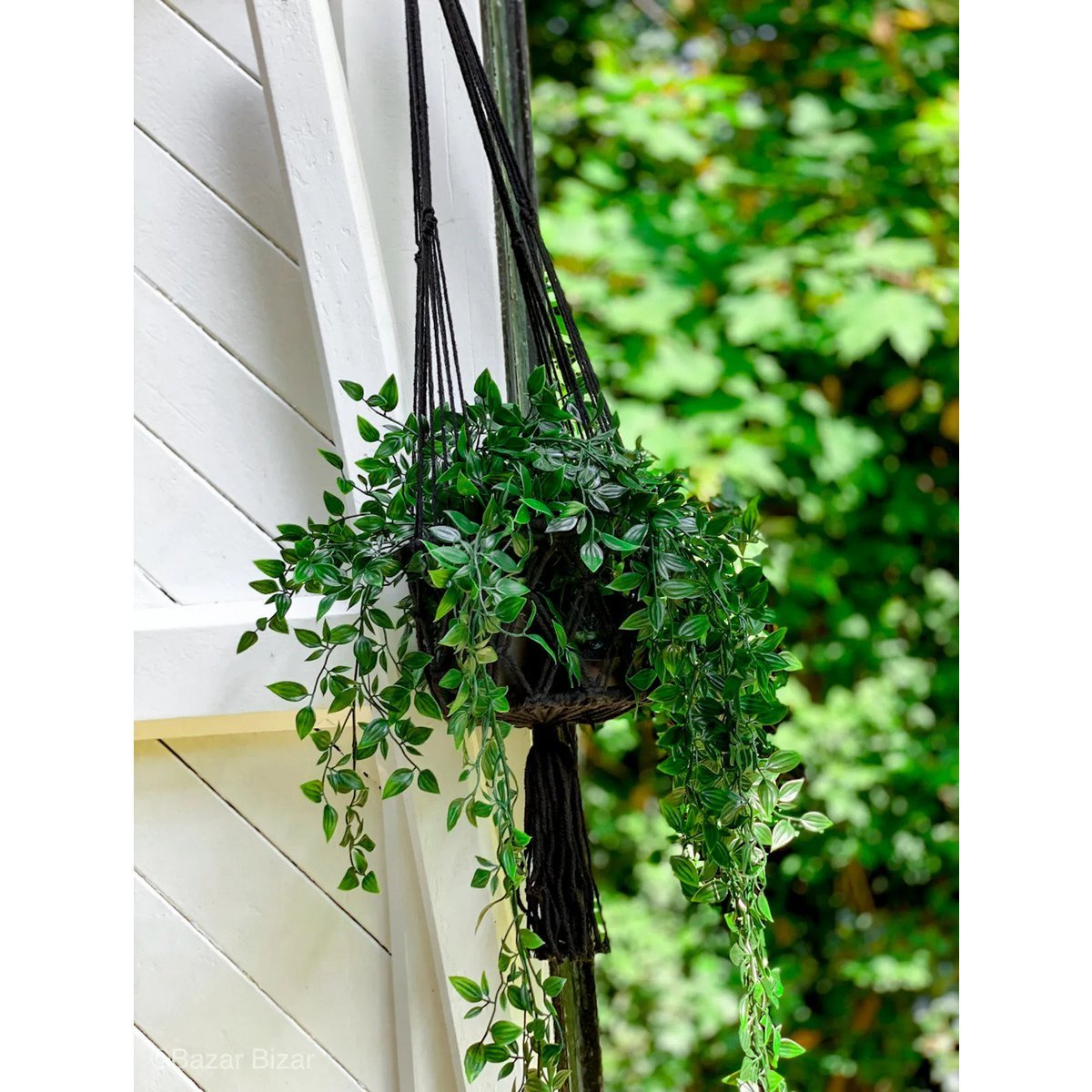 Plantenhanger macramé katoen zwart 110 cm met franjes aan de onderkant in tuin tegen wit houten huis, met groene plantjes erin