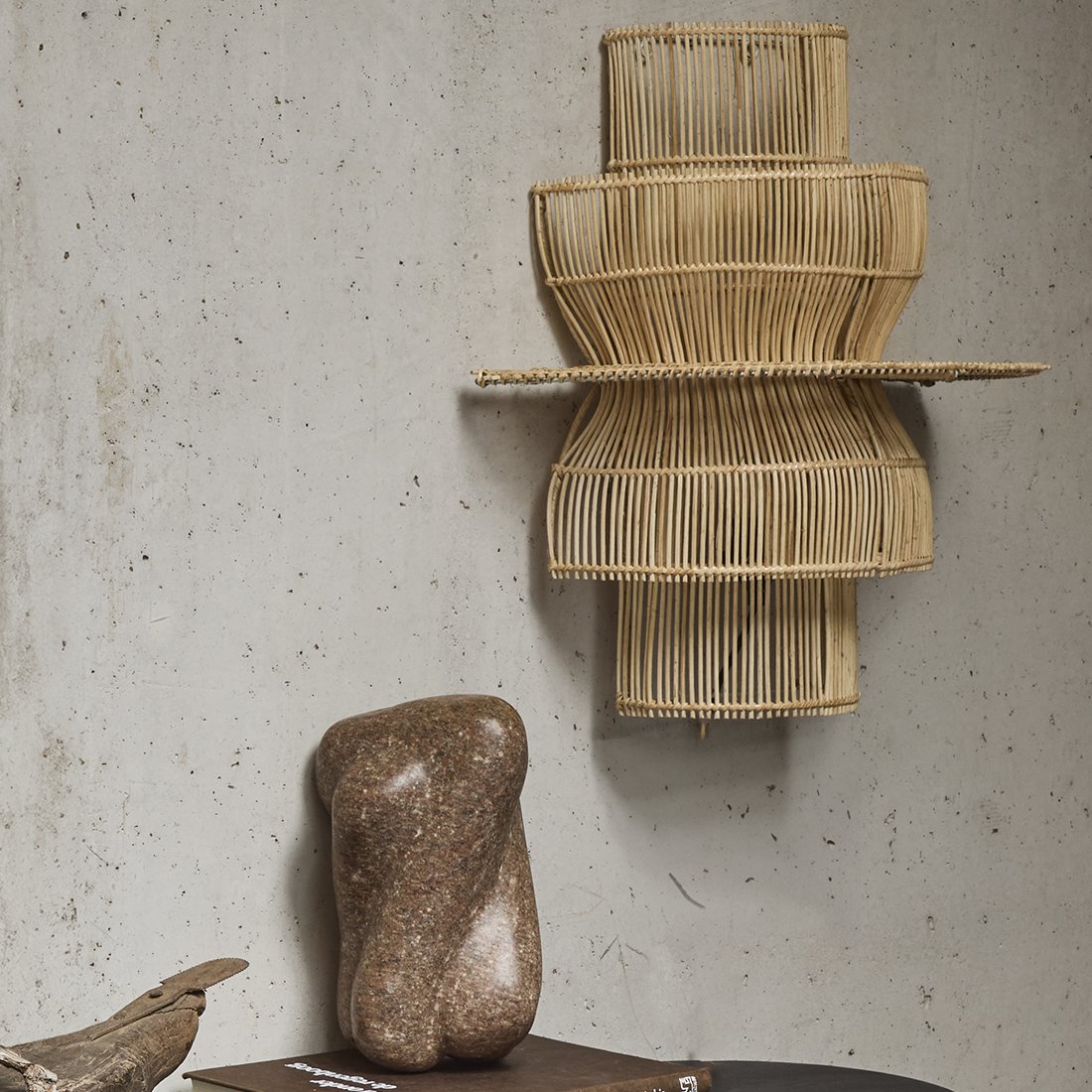 Rotan wandlamp naturel Saturn op een betonnen muur naast stenen decoratie