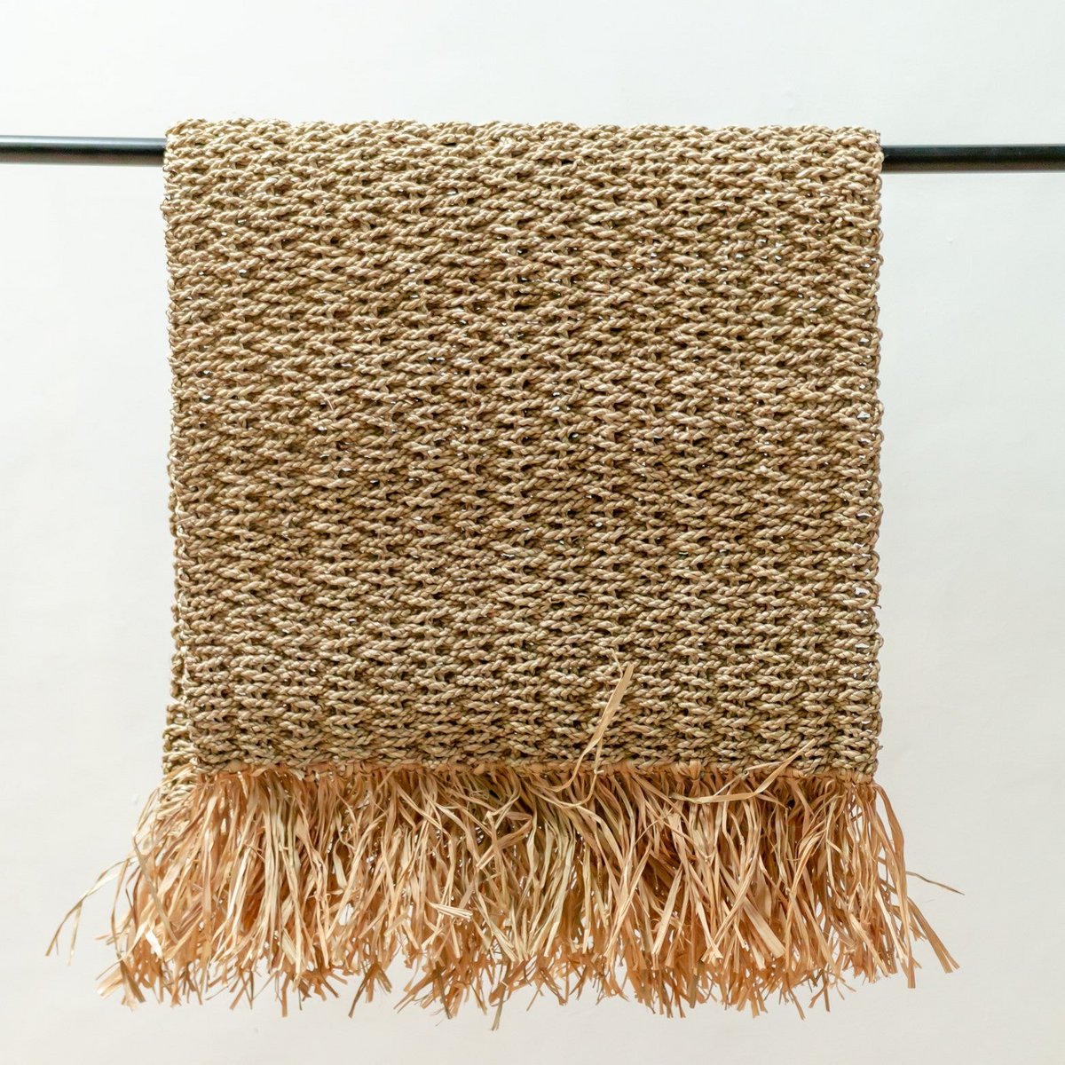 Vloerkleed beige van zeegras met franjes 120x60 cm Bara opgevouwen over een metalen rek