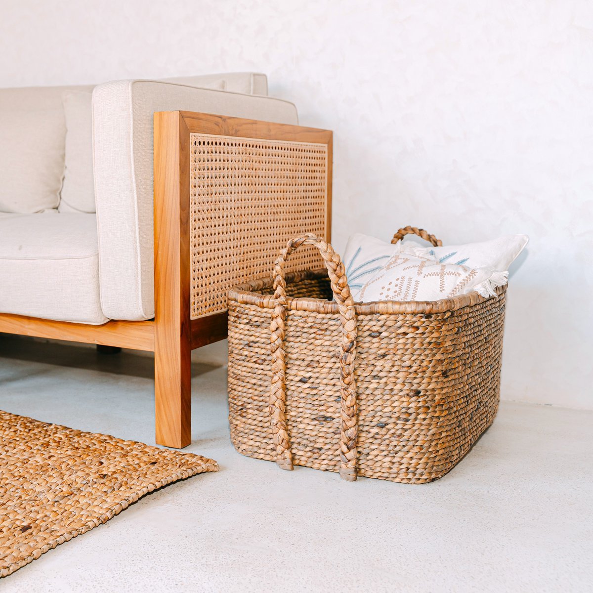 Waterhyacint mand naturel met handvatten Mentari met witte kussens erin naast een rotan bank en geweven vloerkleed