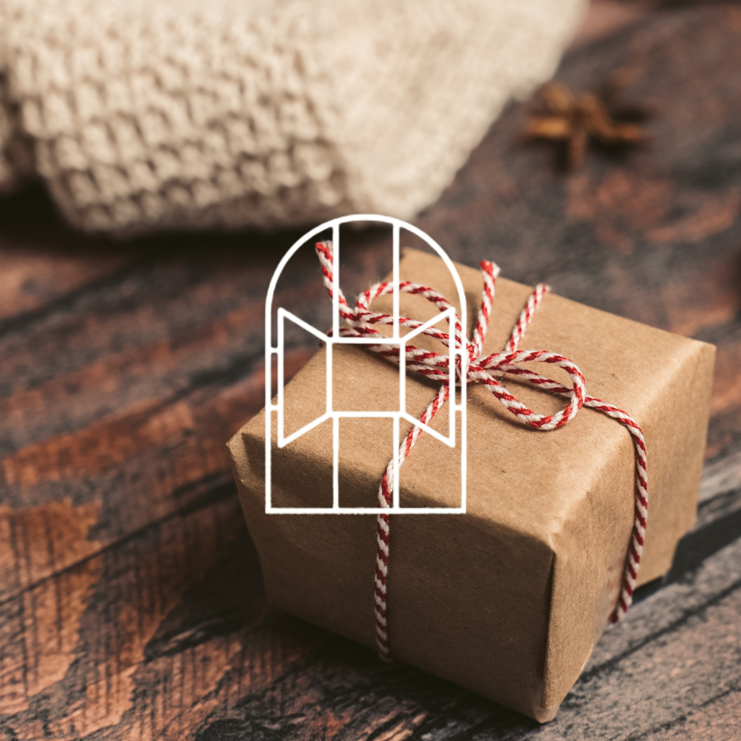 Afbeelding voor de collectie Cadeautips. Op de foto zie je een bruin verpakt cadeautje met rode-witte strik eromheen. Gestyled op een knusse houten tafel voor een warm gevoel.
