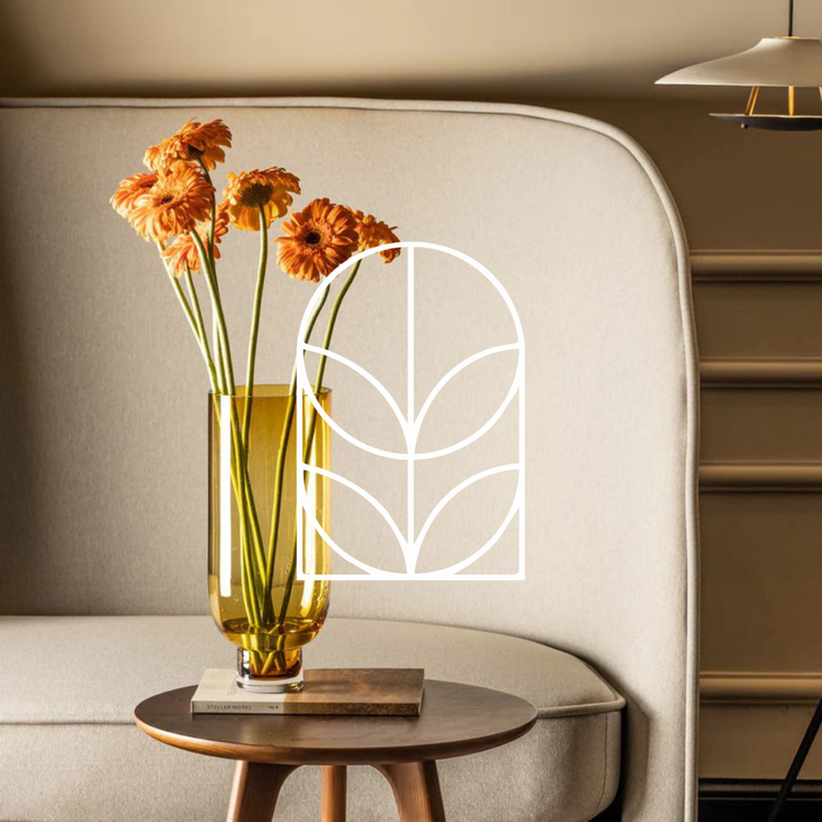 Collectie afbeelding van Groene Cadeautjes, oranje vaas met bloemen op een houten tafel met een witte bank als achtergrond. Het logo staat in het wit op de voorgrond.