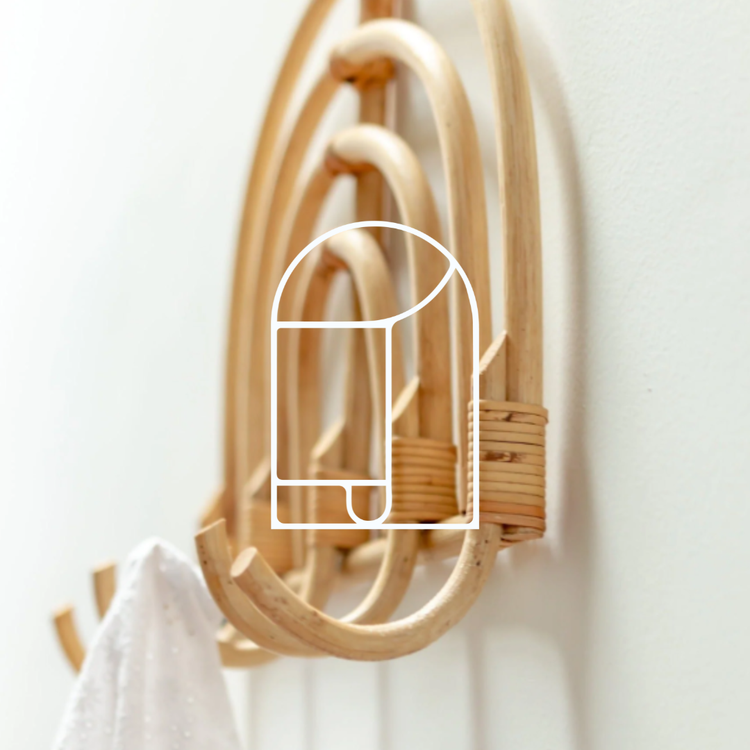 Afbeelding voor de collectie Haken & Kapstokken. Op de afbeelding zie je een rotan kapstok aan een witte wand, met daaraan een witte doek.