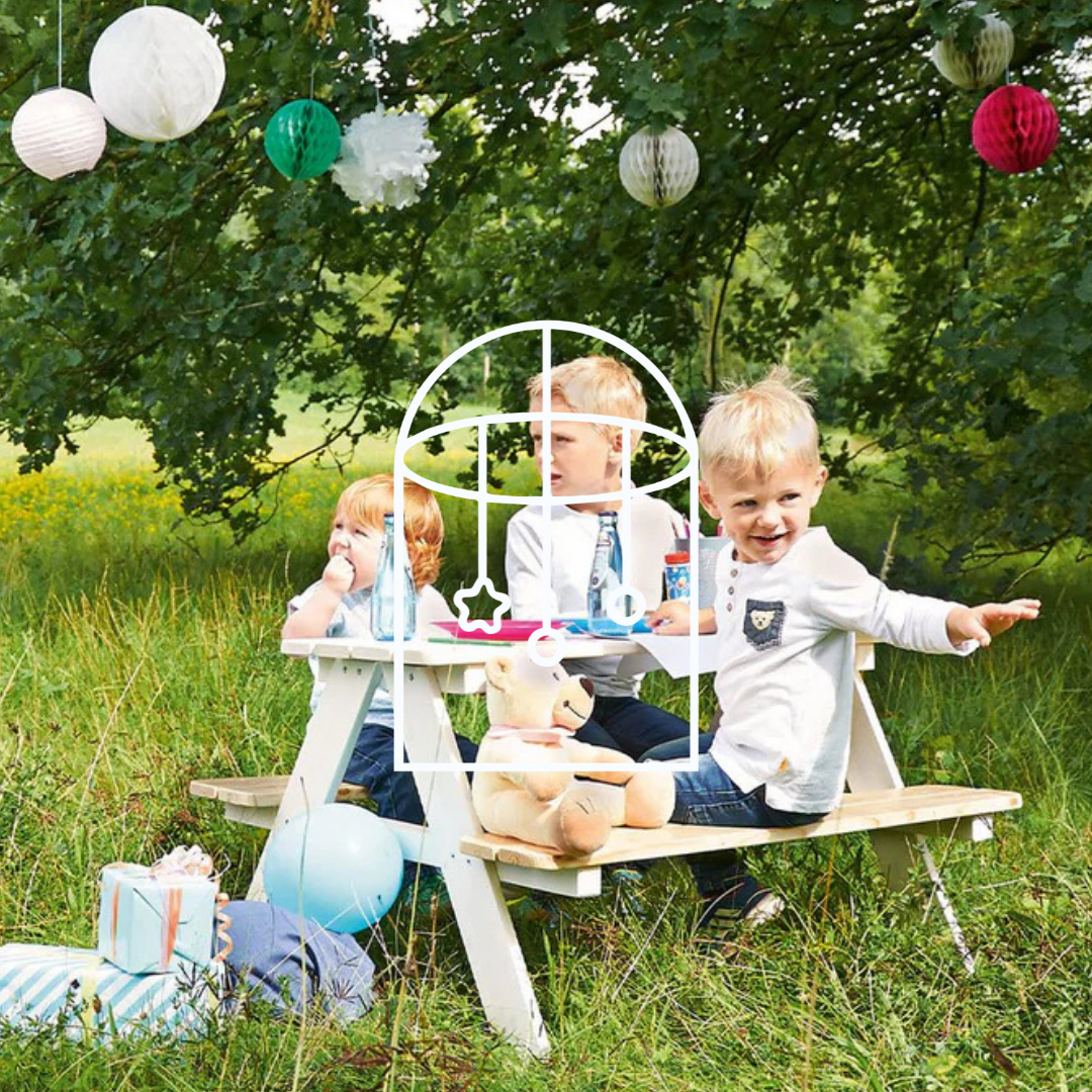 Afbeelding uit de collectie Kindertuinmeubels. Op de foto zie je drie kinderen buiten op een picknickbankje. Er hangen vrolijke lampionnen in de bomen.