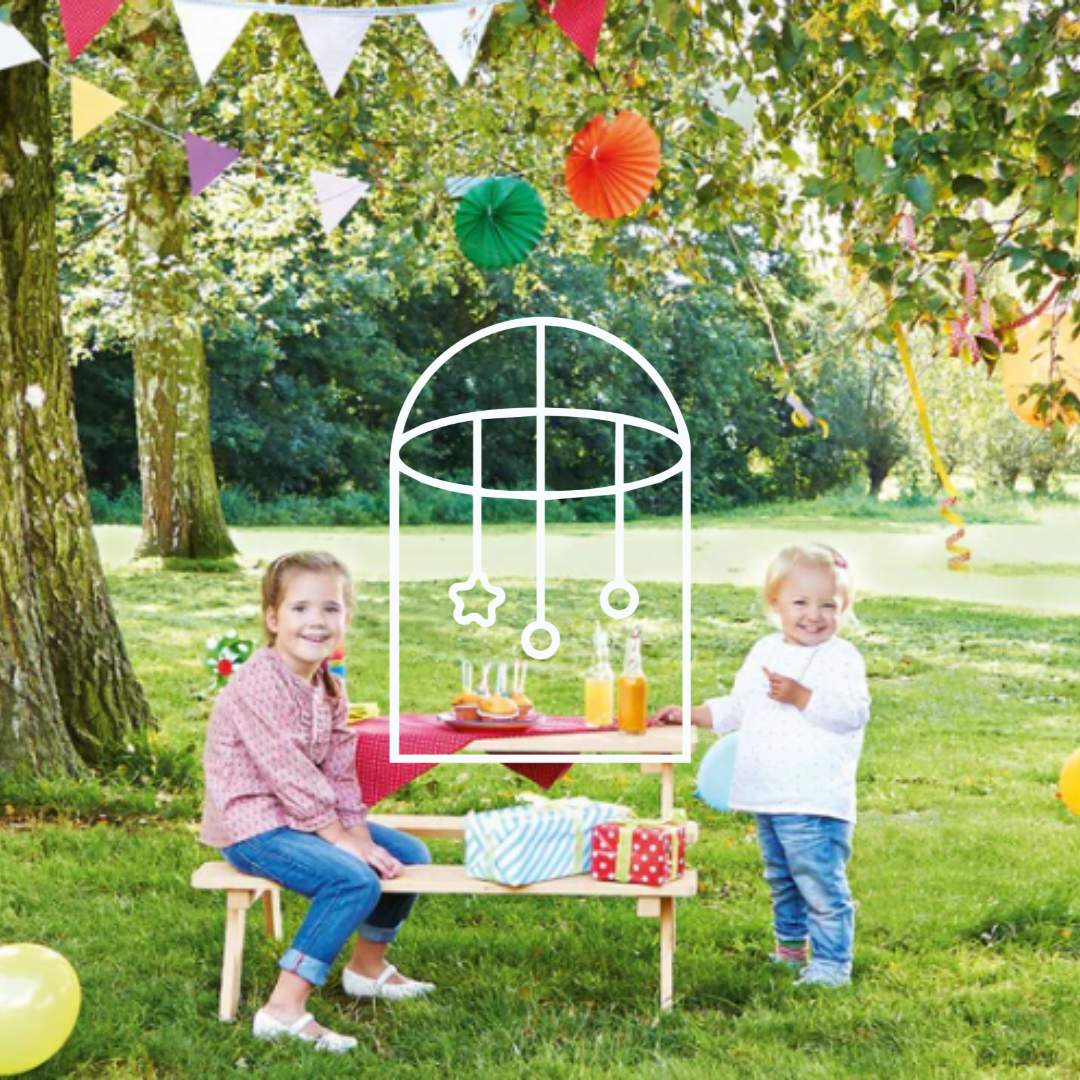 Afbeelding uit de collectie Tuin & Buitenspelen. Op de foto zie je twee kinderen bij een picknickbankje buiten op een groot groen veld. De tafel is leuk gedecoreerd met vrolijke spulletjes.