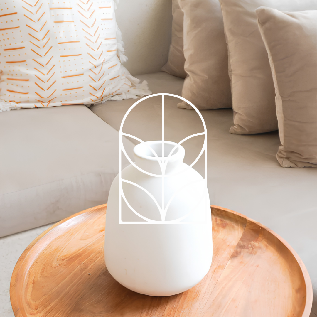 Afbeelding uit de collectie Vazen. Op de foto zie je een witte minimalistische vaas op een houten bijzettafel, met een knusse bank met kussens op de achtergrond.