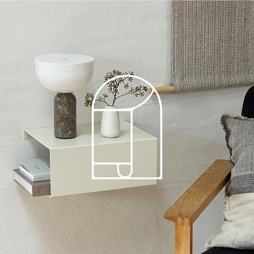 Afbeelding voor de collectie Wandplanken & Wandrekken. Op de foto zie je een witte metalen wandplank, met boeken, vazen en een nachtlamp. 