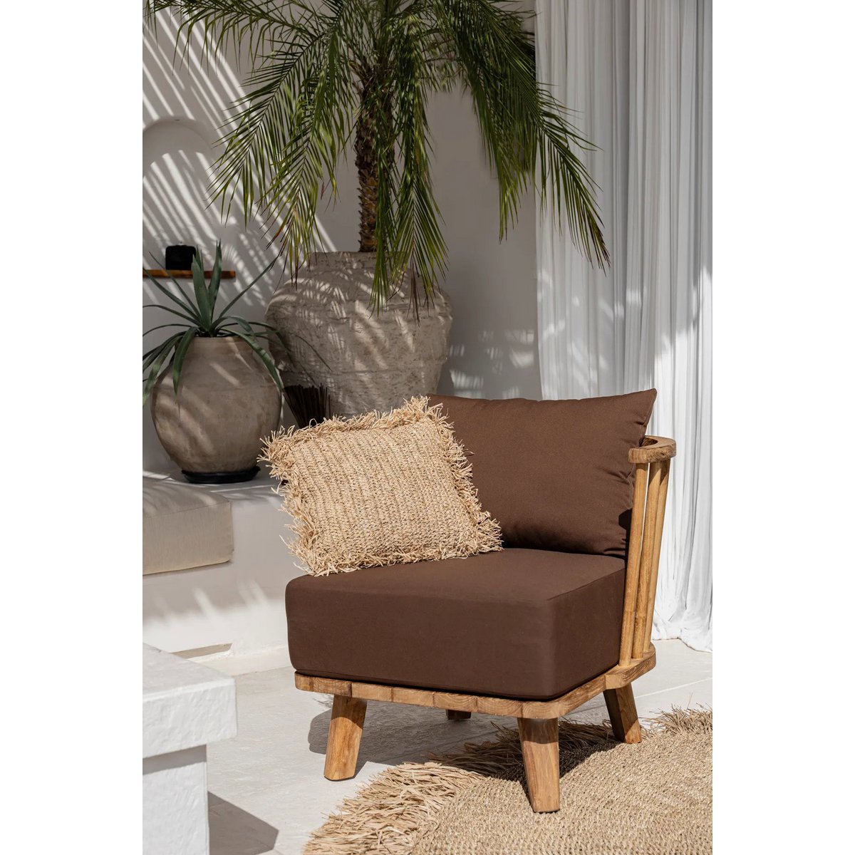 Stylingbeeld met de raffia kussenhoes op een stoel in een lichte ruimte.