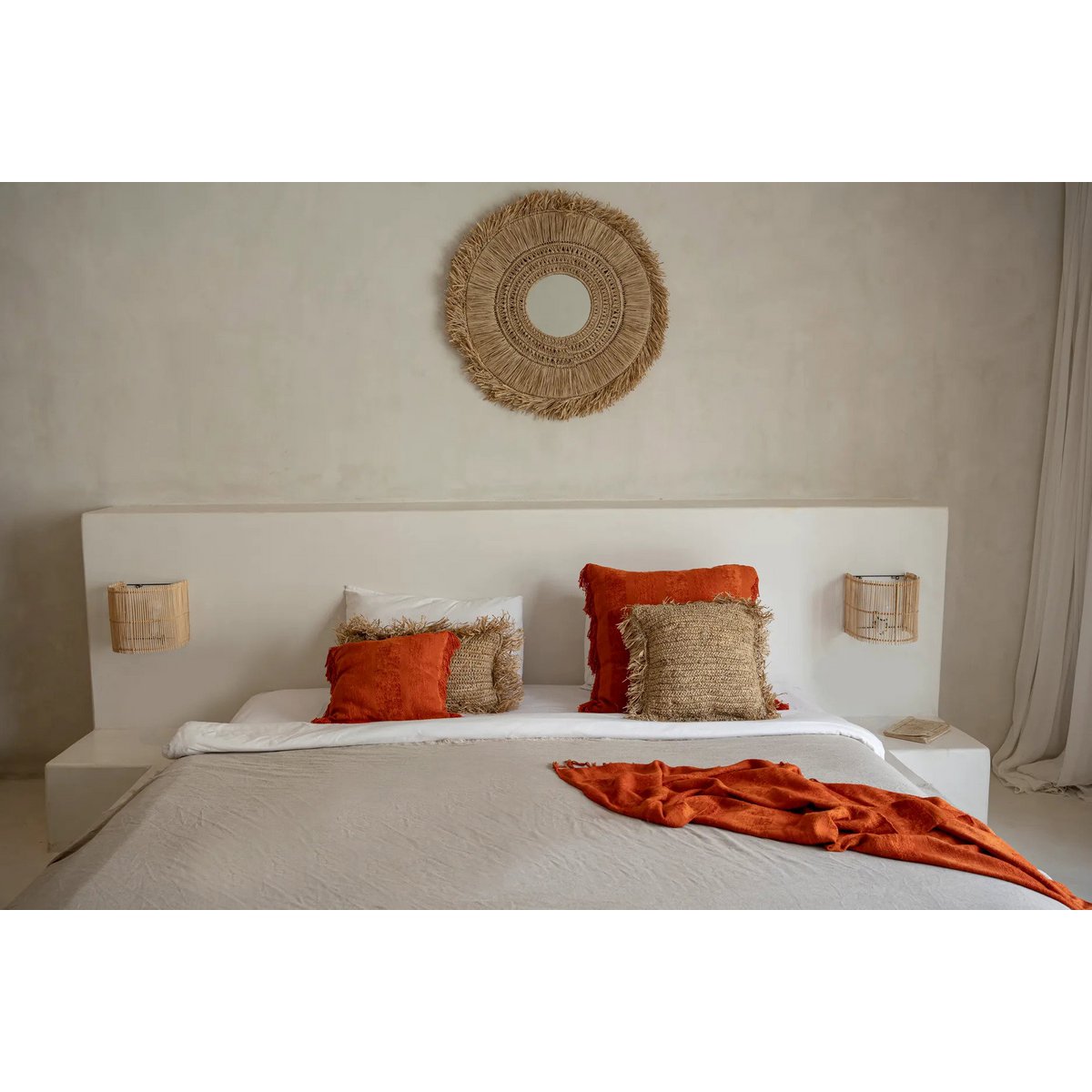 Slaapkamerbeeld met de raffia kussenhoes op een bed samen met andere kussens.