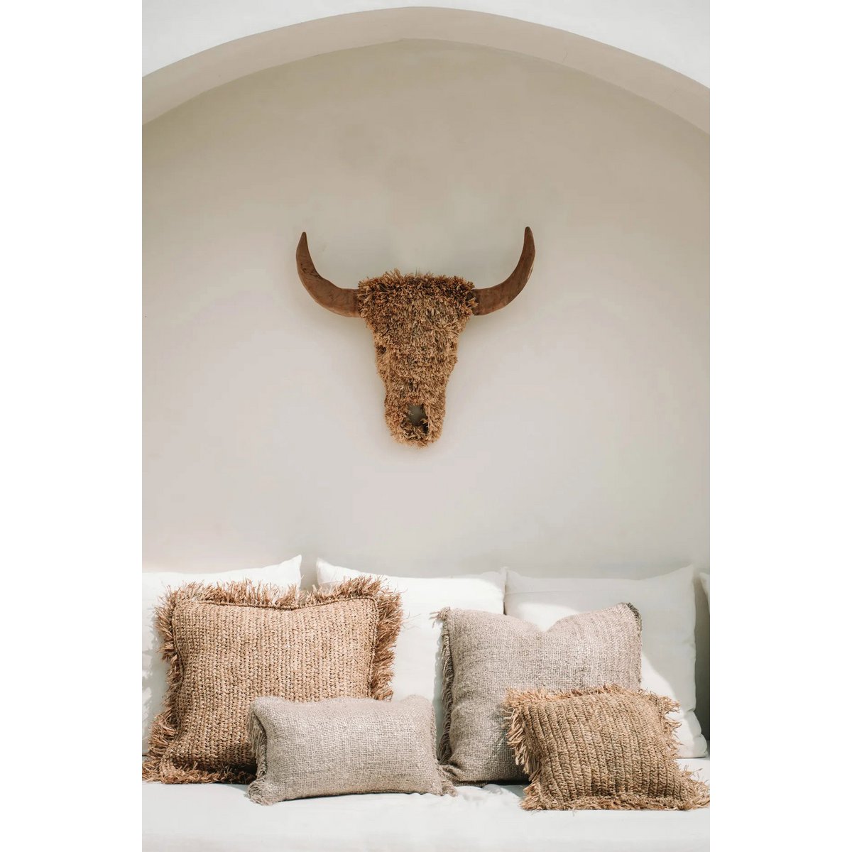 Beige raffia kussenhoes 60 X 60cm gestyled op witte bank onder nep stierenhoofd