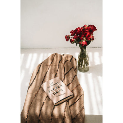 Zachte bruine plaid met zwart detail op bedbank – stijlvolle decoratie voor woonkamer of terras.

