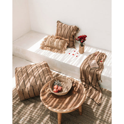 Plaid met franjes op rotan poef – stijlvolle toevoeging aan een boho interieur.