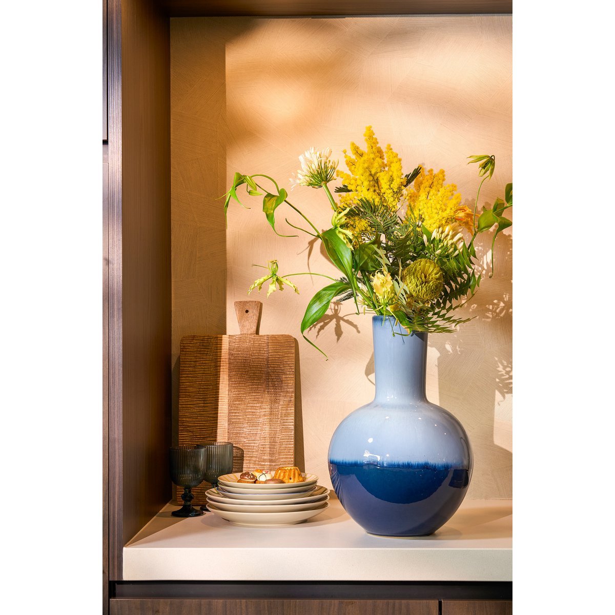 Een blauwe keramieken vaas met een diepe uitstraling, in een landelijke omgeving. Perfect om gedroogde bloemen of takken in te plaatsen, maar ook prachtig als los decoratief object. De diepe tinten en matte afwerking brengen een rustieke en mediterrane sfeer in elk interieur.
