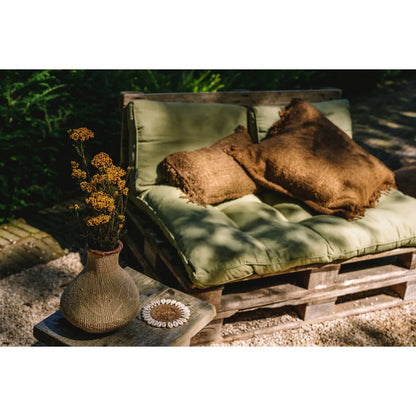 Bruine kussenhoes gestyled op een houten bank met andere boho accessoires in een natuurlijke setting