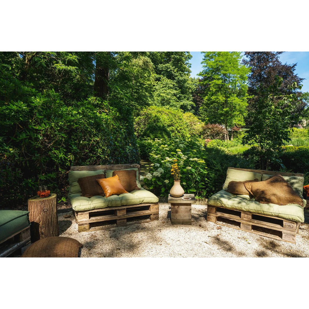 Bruine Oh My Gee kussenhoes buiten gestyled tussen houten decoratie en groen landschap