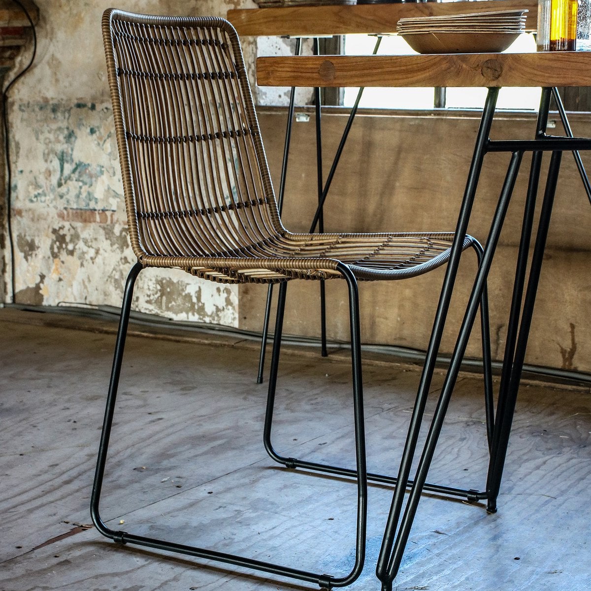De Jane tuinstoel staat naast een houten tafel met zwart metalen frame, in een industriële ruimte met verweerde muren. 