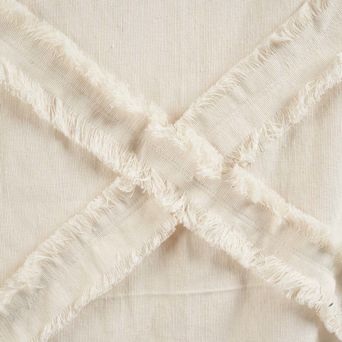 Detail van beige katoenen plaid met gekruiste franjes in X-patroon, gemaakt van zacht en natuurlijk materiaal. Een subtiele en stijlvolle textuur die warmte en een ambachtelijke uitstraling toevoegt aan elk interieur.