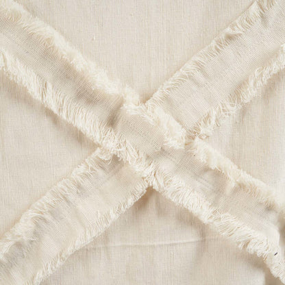 Detail van beige katoenen plaid met gekruiste franjes in X-patroon, gemaakt van zacht en natuurlijk materiaal. Een subtiele en stijlvolle textuur die warmte en een ambachtelijke uitstraling toevoegt aan elk interieur.