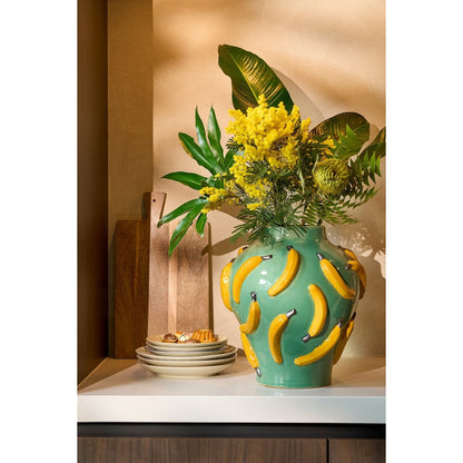Groene keramieken vaas met bananenprint op gestyled met gele en groene bloemen gestyled in een rustige kamer