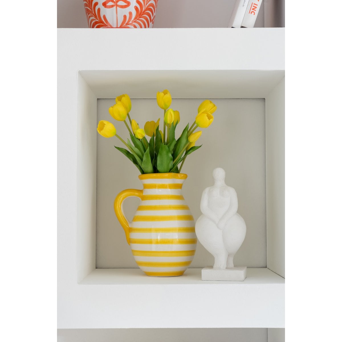 J-Line waterkan keramiek geel gestreept met gele tulpen, naast een wit beeldje in een witte kast