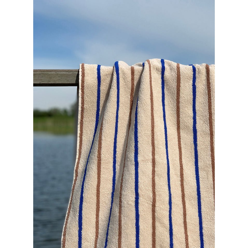 Beige handdoek met blauwe en bruine strepen – luxe badtextiel aan het water.