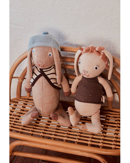 Gebreide knuffel Jolien Rabbit in beige met jurk en hoofdband op rieten stoel