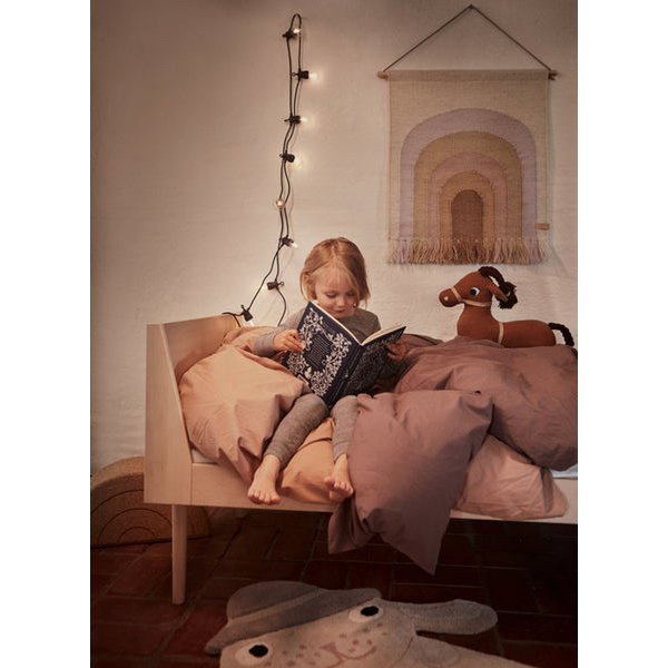 Knuffel geit Taffy naast de kleinere geit, op een bed waar een meisje een boek aan het lezen is