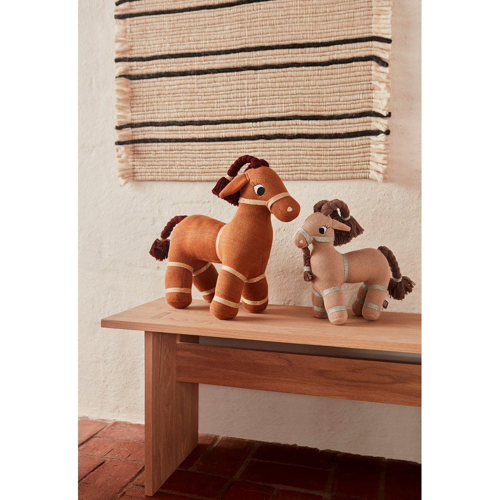 Knuffel geit Taffy naast de kleinere geit, op een houten tafel met rotan gordijnen aan de muur
