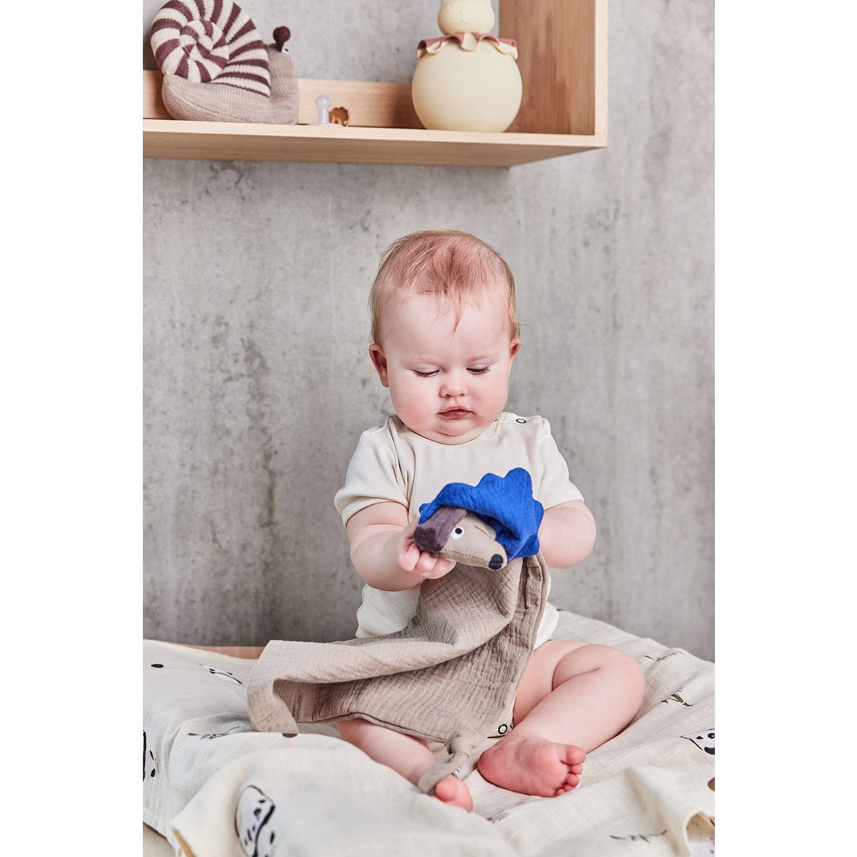 Kind zit op een plank met het beige konijn-nachtlampje op de achtergrond in de kinderkamer.