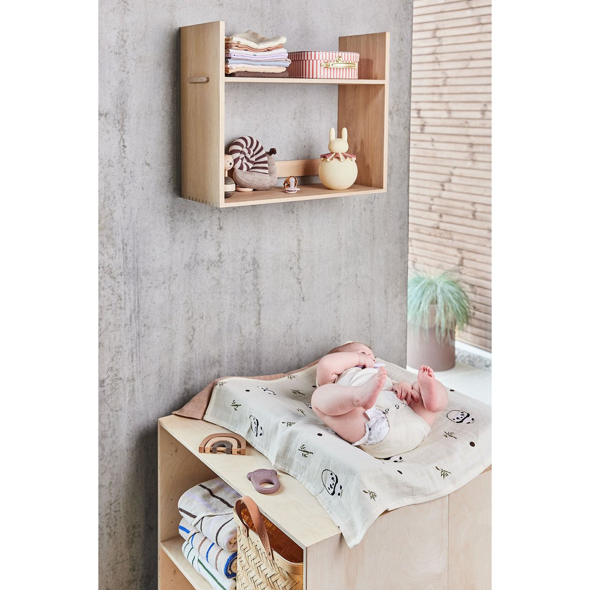 Beige konijn-nachtlampje op een plank boven een commode in een lichte kinderkamer.