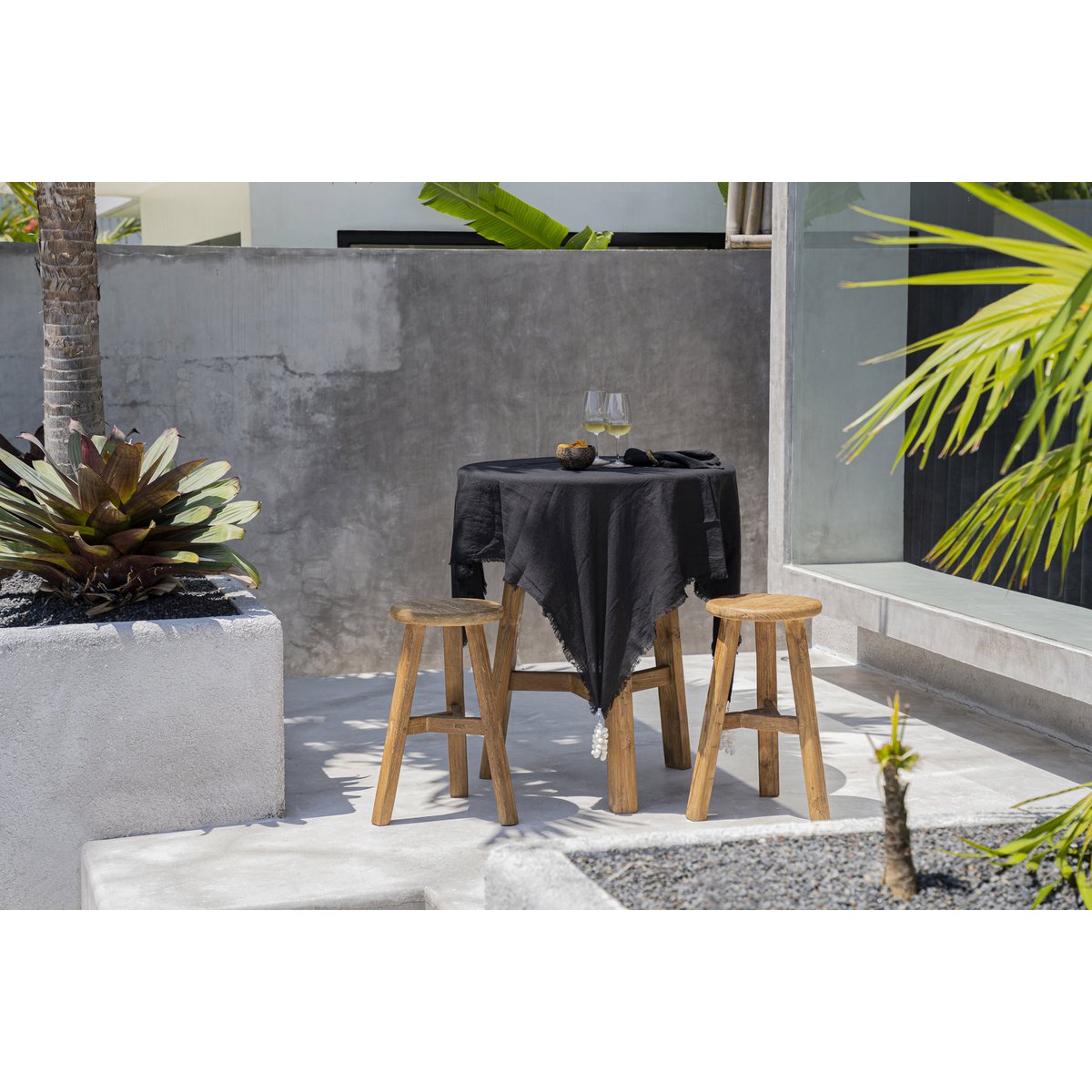Linnen tafelkleed zwart 150x150 cm in een tuin over houten ronde tafel met glazen en schalen en groene planten in pottenA