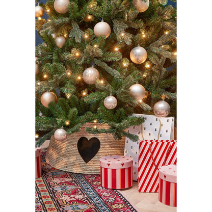 Rotan kerstboommand met zwart hart – stijlvolle basis onder een versierde kerstboom met geschenken.

