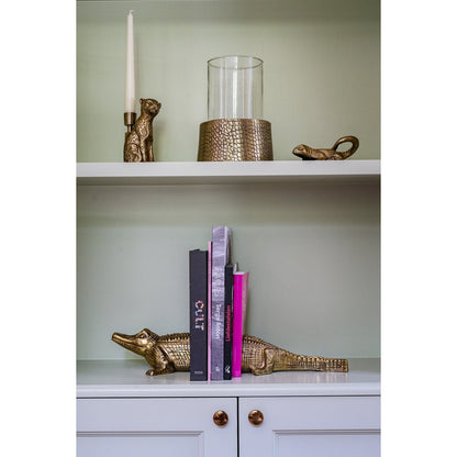 Goudkleurige kaarshouder op witte kast met boeken en accessoires – stijlvolle woondecoratie in luxe design.
