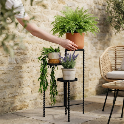 Plantenstandaard zwart metaal hoog 70 cm Salvo met verschillende formaten plantenpotten en planten erin in een sfeervolle tuin