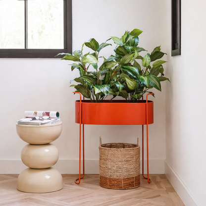 Rode metalen plantenbak Moritz met een plant erin, over een boho mand en beige bijzettafel