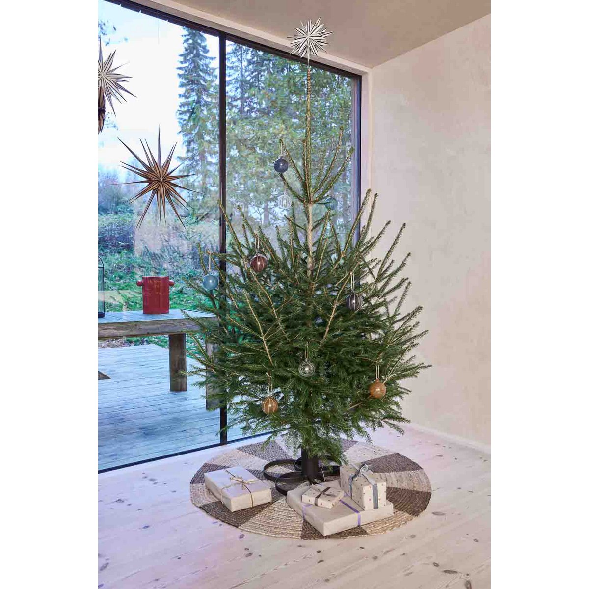 Versierde kerstboom op zwarte metalen standaard – minimalistische kerstdecoratie in lichte woonkamer.

