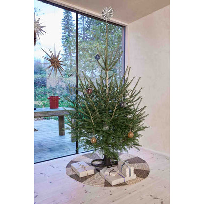 Versierde kerstboom op zwarte metalen standaard – minimalistische kerstdecoratie in lichte woonkamer.
