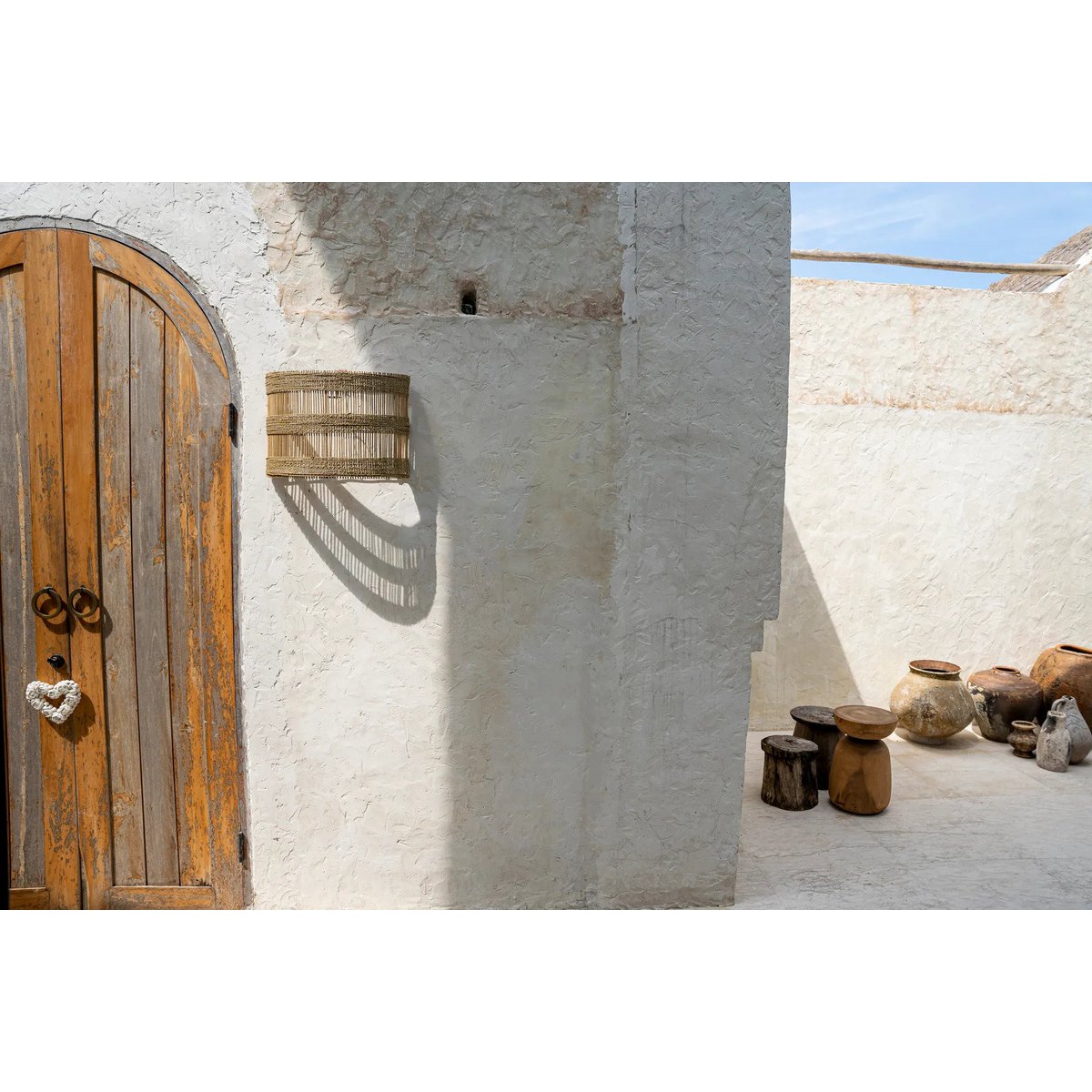 Doedoe rotan wandlamp gemonteerd naast een houten deur in mediterrane setting