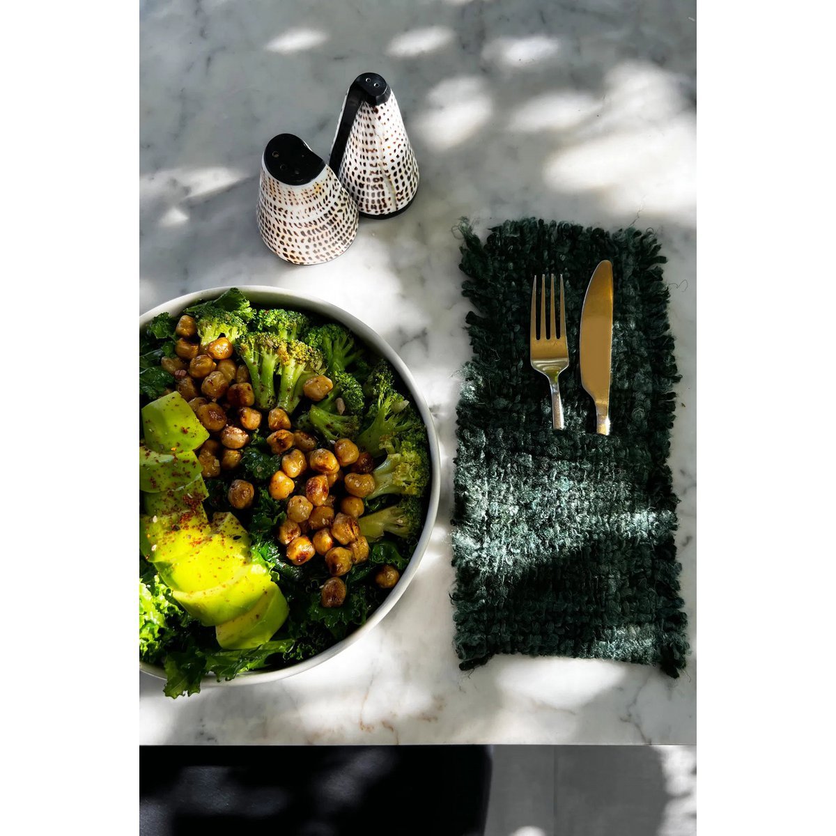 Schelpen zout- en peperstel op een marmeren tafel naast een groene salade en bestek.