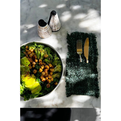 Schelpen zout- en peperstel op een marmeren tafel naast een groene salade en bestek.