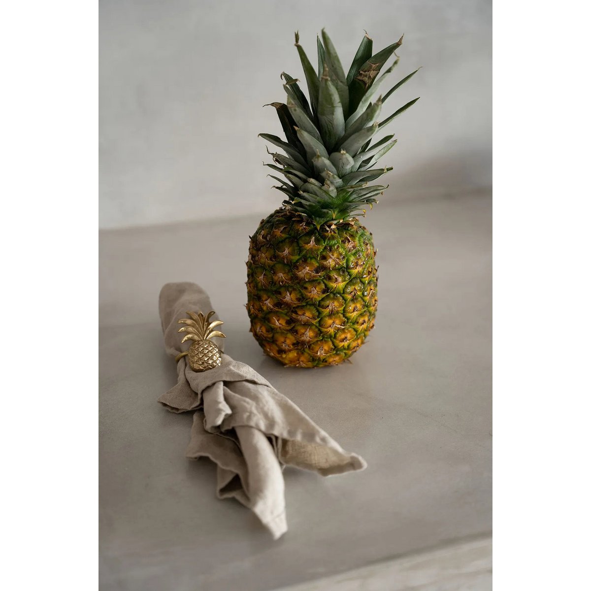 Servetring goud ananas om een beige servet naast een grote ananas