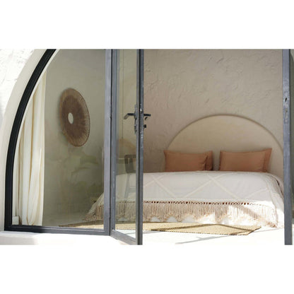 Beige katoenen plaid met decoratieve franjes op een bed in een lichte, serene slaapkamer met natuurlijke tinten. Een elegant en zacht woonaccessoire dat warmte en textuur toevoegt aan een bohemian of mediterraans interieur.