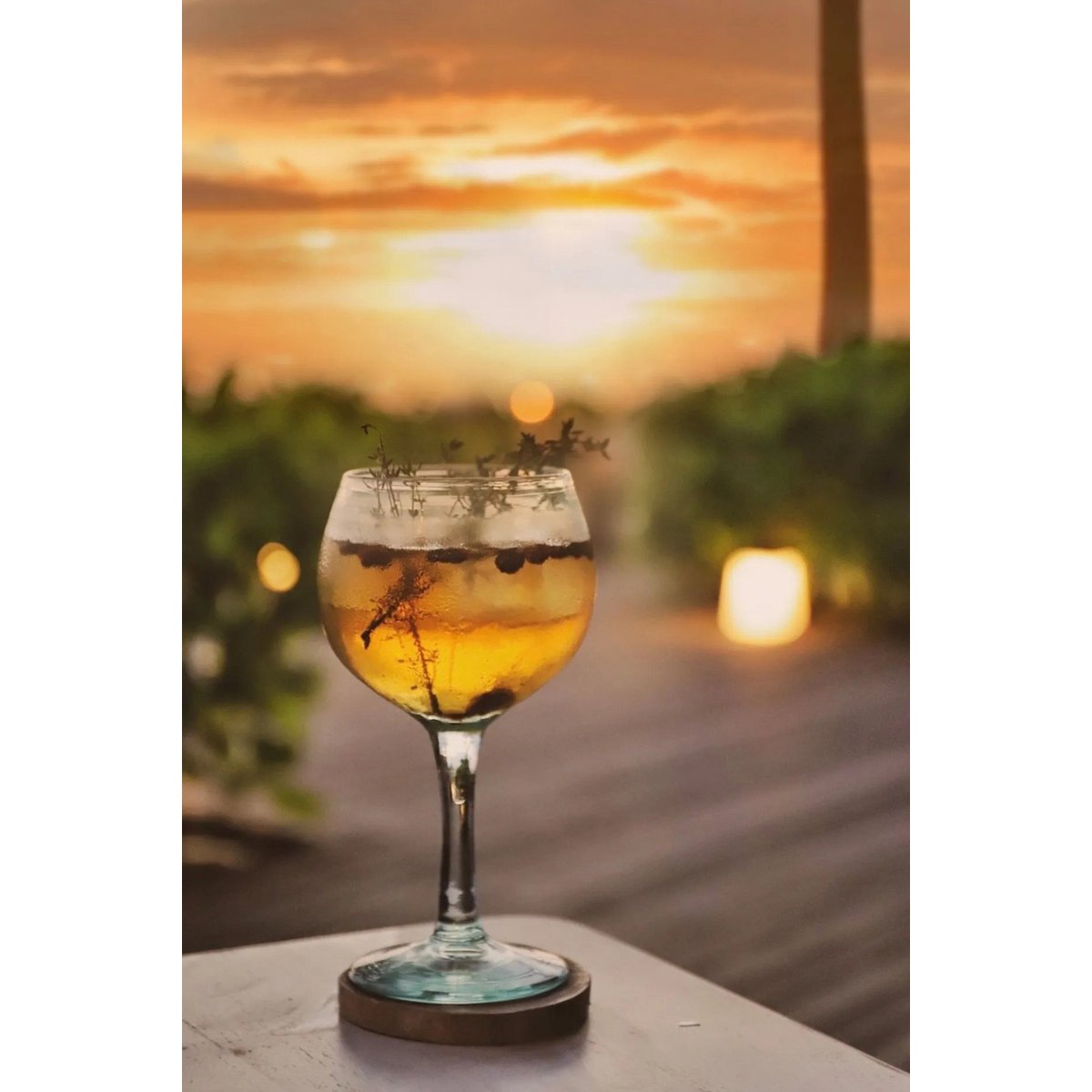 Teakhouten onderzetter met een cocktail glas erop met druiven, op de achtergrond is de zonsondergang