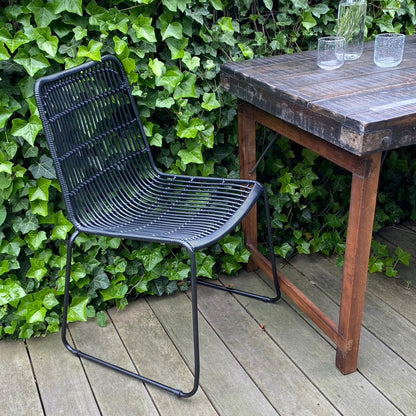 Tuinstoel rotan zwart Jane op terras aan donkere houten tafel tegen een beplante muur