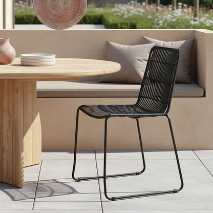 Tuinstoel rotan zwart Jane op terras aan houten tafel met een beige bank op de achtergrond
