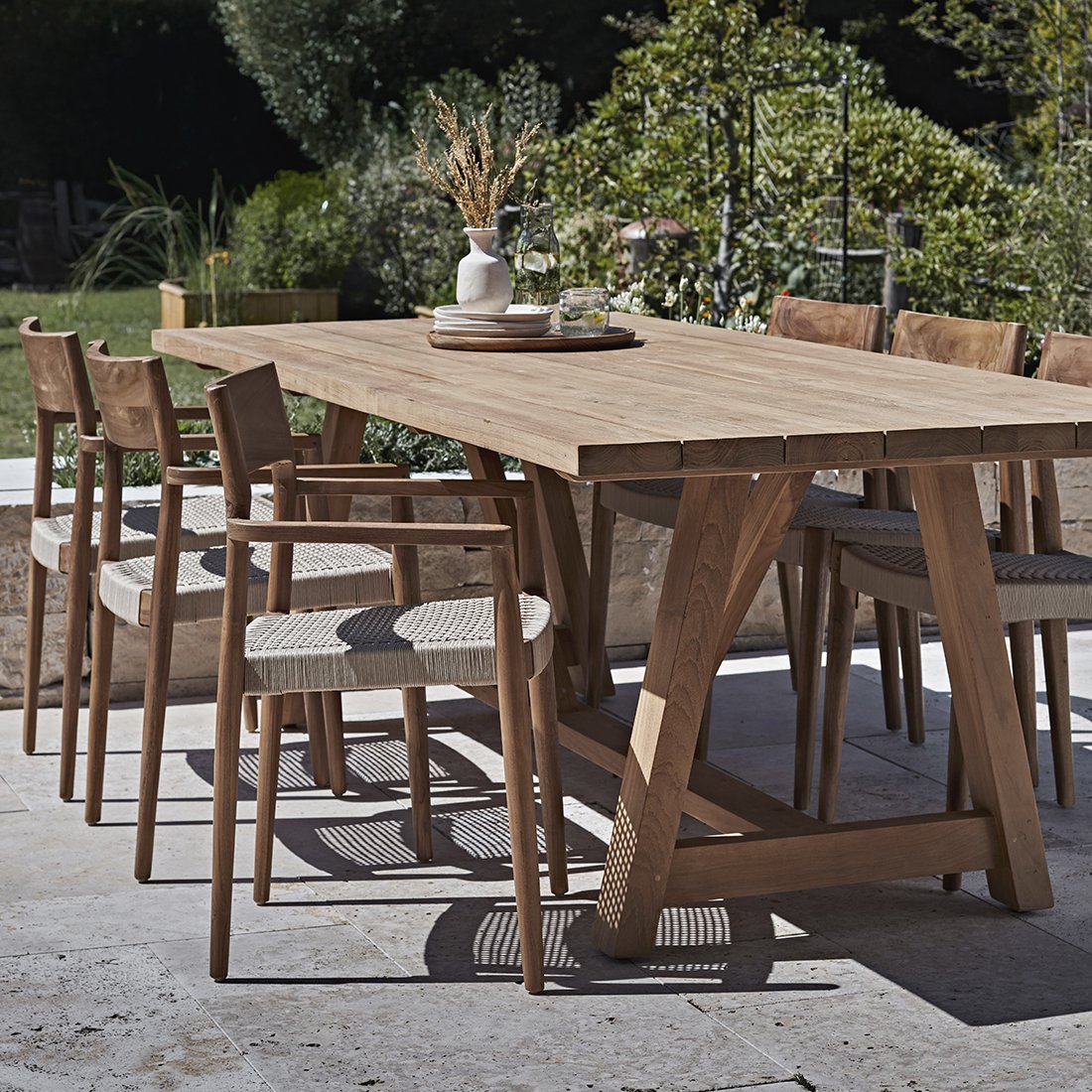 Tuinstoel teak donker met armleuning Freya in tuin aan grote tafel en meerdere stoelen