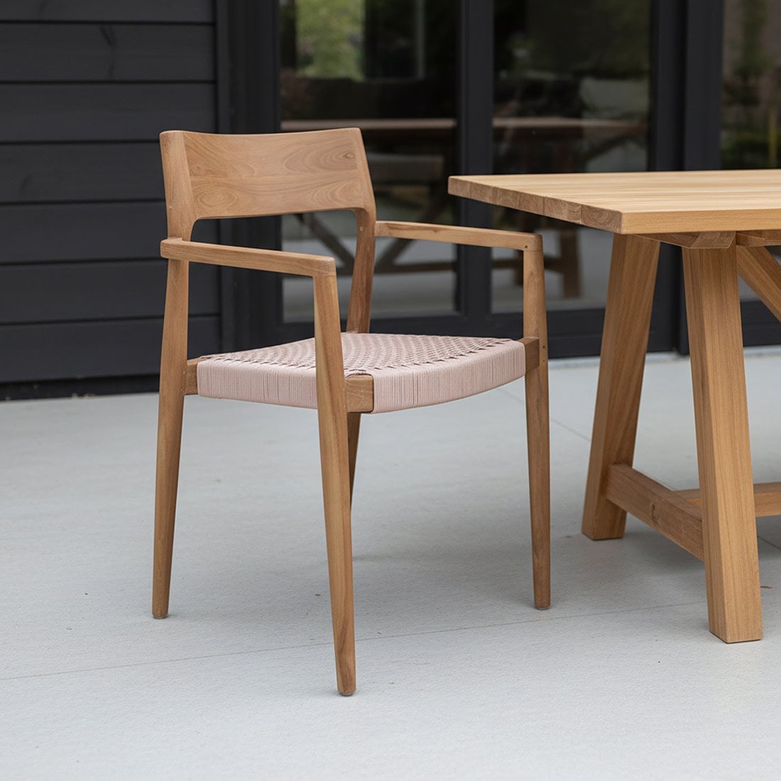 Tuinstoel teak donker met armleuning Freya op veranda met een houten tafel ernaast