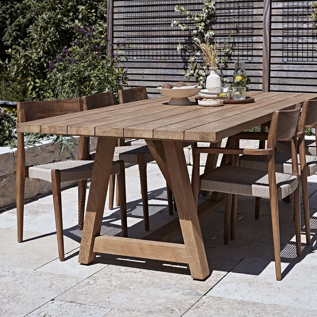 Tuinstoel teak donker naturel Freya met andere stoelen aan teakhouten tafel met decoratie