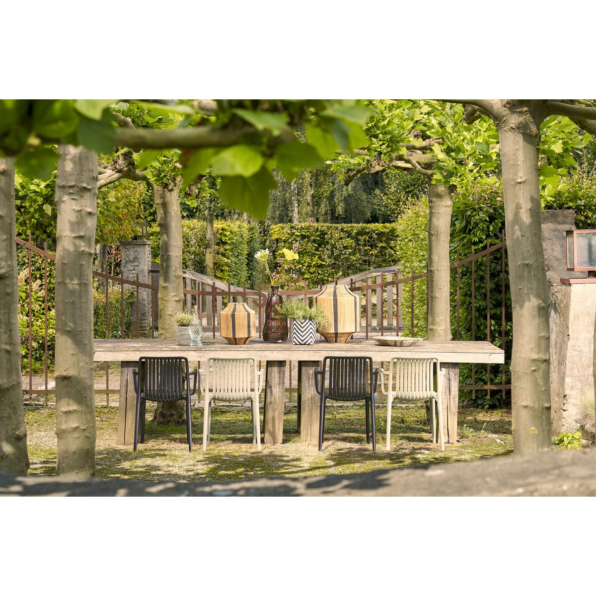 Tuinstoel zwart met armleuningen 53x77,5 cm Paloma in een tuin met dezelfde stoelen in een andere kleur. De tafel is gedekt met vazen en plantjes